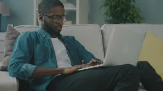 man in denim shirt surfing the web on a white couch